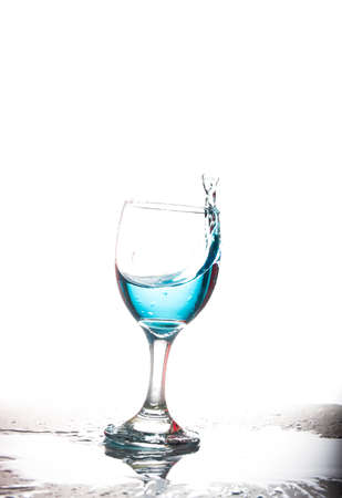 Splashing blue water into the crystal wine glass, closely spreading on a white background.の写真素材