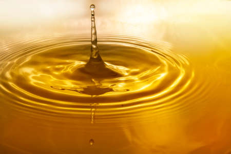 Drops of water on the surface of the water spreading and forming waves, reflecting the beautiful light from the golden evening light.の写真素材