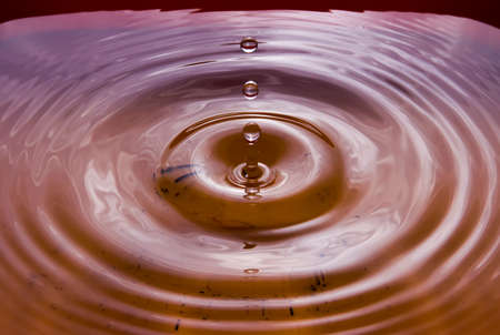 Water droplets falling on the water surface create beautiful ripples on the orange water surface.の写真素材
