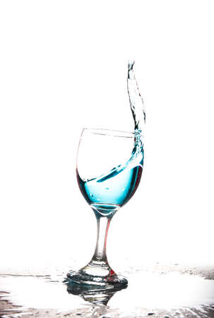 Splashing blue water into the crystal wine glass, closely spreading on a white background.の写真素材