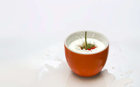 Strawberries fell into the milk in an orange glass until the milk spread beautifully on a white background.の写真素材
