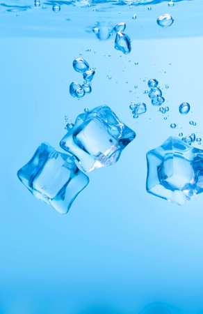 Ice cubes in blue water create bubbles that float to the surface, blue liquid.の写真素材