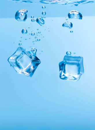 Ice cubes in blue water create bubbles that float to the surface, blue liquid.の写真素材