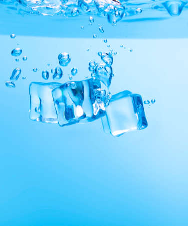 Ice cubes in blue water create bubbles that float to the surface, blue liquid.の写真素材