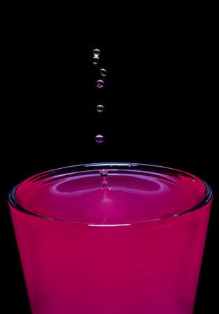 Beautiful drops of water fall on a glass of bright pink water. Create swaying water waves on a black background.の写真素材