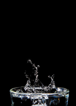 The image of the swaying water is not clear. Splashing water on glass on isolated black background with close-up details side view Clear glass with liquid. Hand over the glass.の写真素材