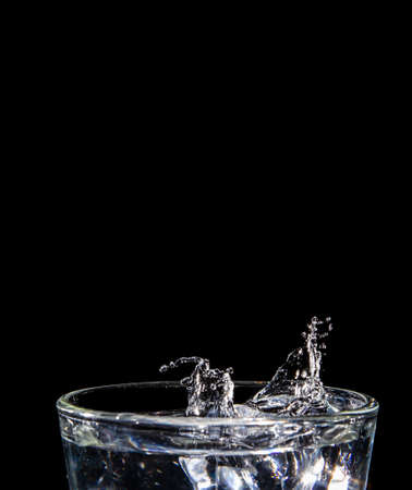 splashing water into glass on black background isolated with close-up details side view Clear glass with liquid. Hand over the glass.の写真素材