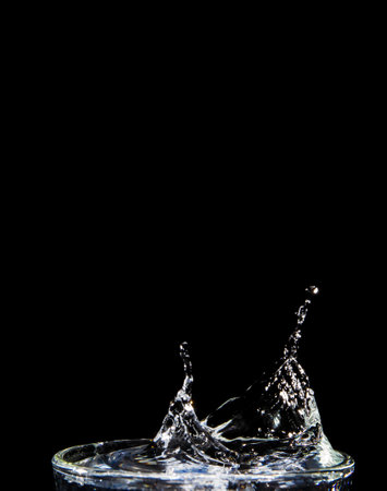 The image of the swaying water is not clear. Splashing water on glass on isolated black background with close-up details side view Clear glass with liquid. Hand over the glass.の写真素材