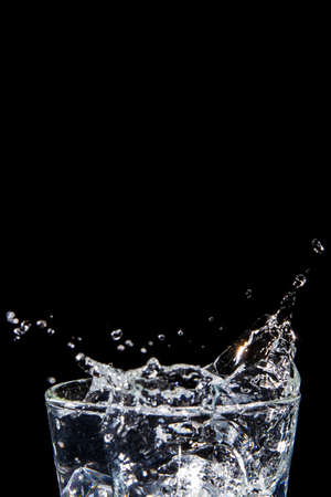 The image of the swaying water is not clear. Splashing water on glass on isolated black background with close-up details side view Clear glass with liquid. Hand over the glass.の写真素材