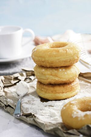 Homemade fried donuts or cronuts in stack with sugar standing on crumpled paper over white wooden concrete table.の写真素材