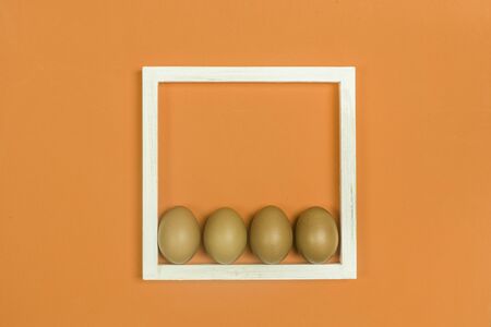 Eggs and white wooden frame on an orange backgroundの写真素材