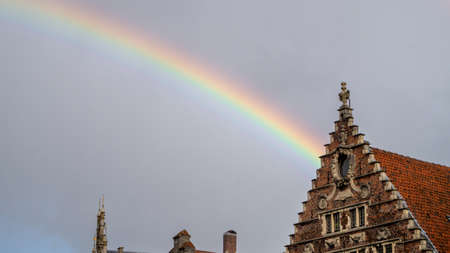 Rainbow with cloudy sky, with a Belgian house next to it.の写真素材
