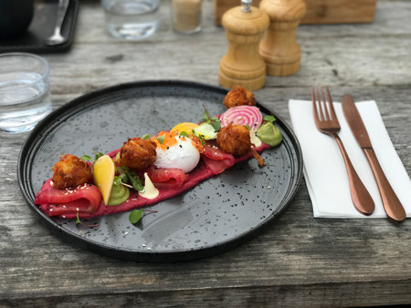 Beetroot salad with poached egg on black plate on wooden table