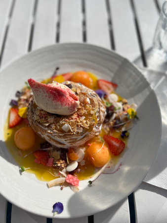 Pancakes with fruits and berries on a white wooden table.
