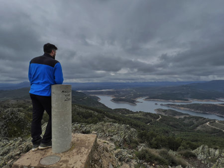 Man on the top of the mountain looking at the valley and the lakeの写真素材