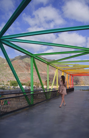 Young woman standing on the bridge over the sea and looking at the mountainsの写真素材