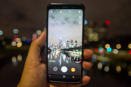 A man using a smartphone to take a photo of the city at night.