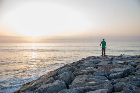 Man standing on a rock and looking at the sea in the sunsetの写真素材