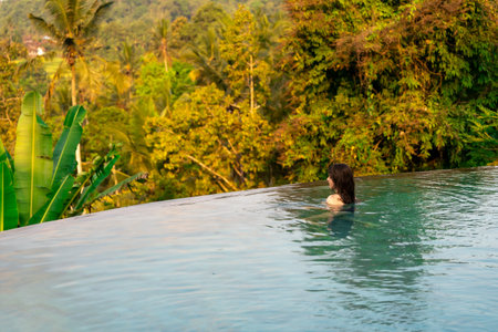 Back view of young woman relaxing in swimming pool at tropical resort.
