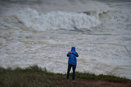 A boy in a blue jacket stands on the shore of a stormy seaの写真素材