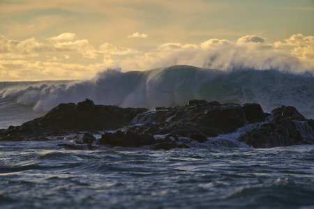 Huge wave breaking on the rocks at sunset. Natural background.
