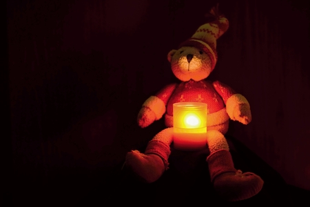 Beautiful Christmas teddy bear sitting with candle. Seasonal winter background for Christmas and holidays. Black clean background with copy space.の写真素材