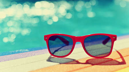 Summer background. Concept for summer and vacation. Red sunglasses by the pool in the background...