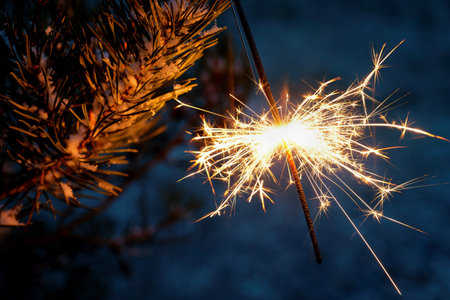 Christmas background. A sparkler on a Christmas tree in the evening outside with snow. Concept for winter season, holidays and new year 2023.の写真素材