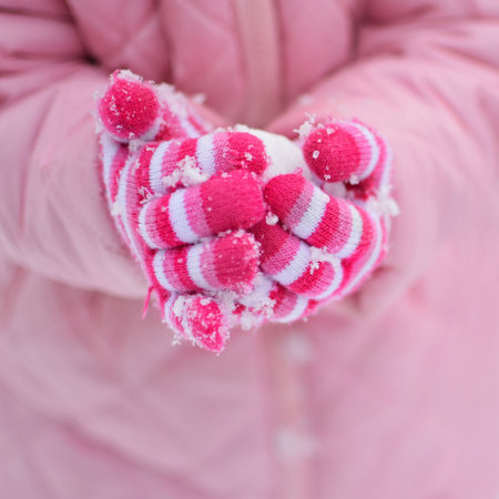 A girl in a pink jacket holds her hands in the snow.の写真素材