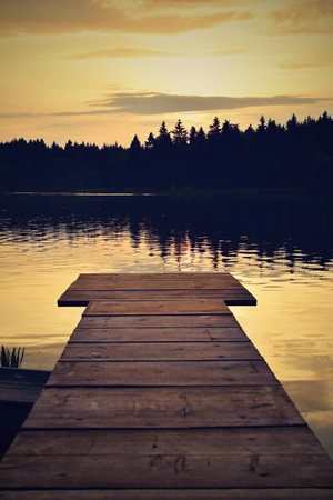 Wooden pier on a lake at sunset with a forest in the backgroundの写真素材