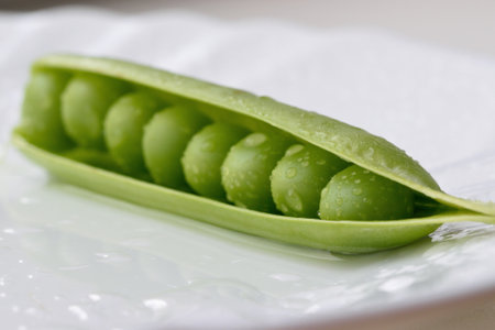 Fresh green pea pod with water droplets on a white plate