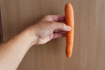 Female hand holding a carrot on a wooden background. Close-up.の写真素材