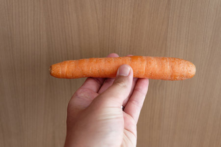 Hand holding a fresh carrot on a wooden background, top view.の写真素材