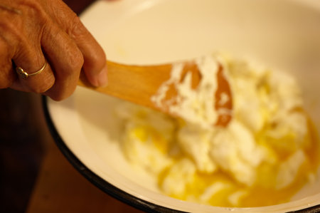 Close-up of a woman's hand mixing eggs in a bowl.の写真素材