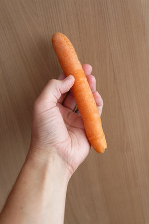 Female hand holding a fresh carrot on a wooden background, top viewの写真素材