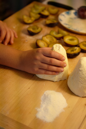 Child's hands knead dough on a table with plums.