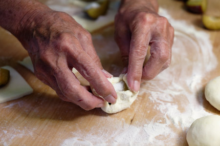 Hands of an elderly woman kneading dough on a wooden board