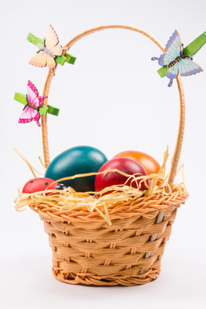 Colorful Easter eggs decorated with butterfly and ladybug  in the wicker basket on white backgroundの写真素材