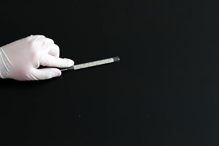 A hand in a medical glove holds a thermometer on black background