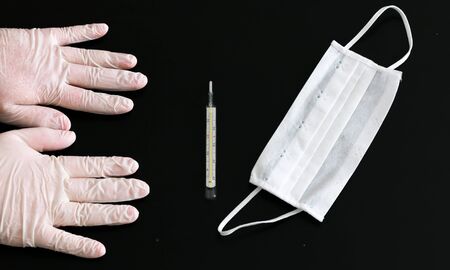 Two hands in latex gloves, thermometer and medical mask close-up on black backgroundの写真素材