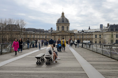 Paris, France - March 20, 2023: People at pedestrian the Arts bridge with views to the domed building of the Institut de France in Paris, France.のeditorial素材