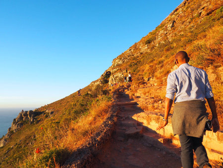 African man hiking on the way to on top of Lion's Head mountain during gold light sunset with navy blue sky background in Cape Town, South Africa, Table Mountain national park.のeditorial素材