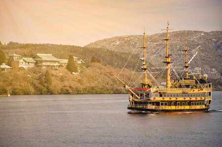 Sightseeing Pirate ship sailing in the sea near Japan old village with the mountain background.