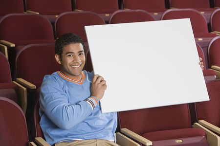 Man sitting in auditorium, holding empty placardの写真素材