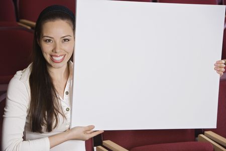 Woman sitting in auditorium, holding empty placardの写真素材