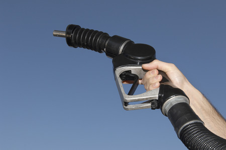 Person holding fuel pump against blue sky, close-up