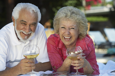Portrait of senior couple relaxing in garden with wine and laughingの写真素材