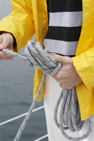 Young man tying rope on yacht, mid section