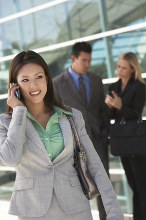 Businesswoman using mobile phone with colleagues in background, outdoorsの写真素材