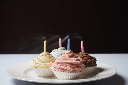 Colourful cupcakes with blowed birthday candles on plateの写真素材